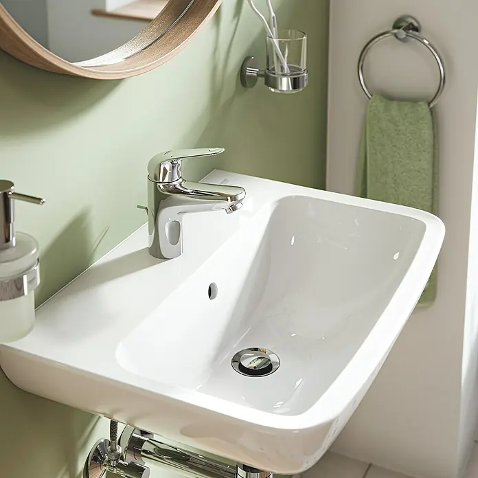 Grohe QuickFix Waschtischarmatur Swift - Chrom, Glänzend, Höhe: 162 mm - Detailaufnahme eines modernen weißen Waschbeckens mit Armatur, Seifenspender und Handtuchring in einem stilvollen Badezimmer.