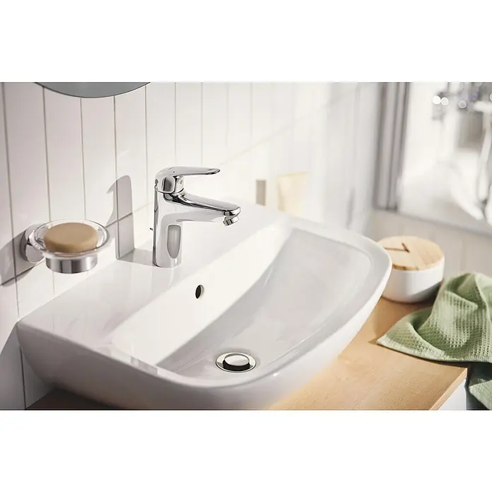 Grohe QuickFix Waschtischarmatur Swift - Chrom, Glänzend, Höhe: 162 mm - Nahaufnahme eines modernen Badezimmerwaschbeckens mit Armatur, Seife und Handtuch. Das Waschbecken ist weiß und hat eine ovale Form.