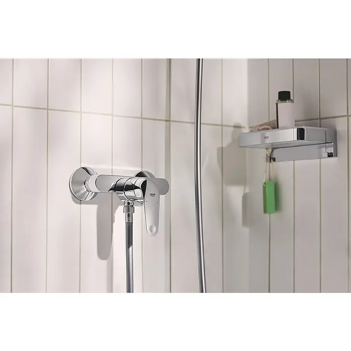 Grohe QuickFix Duscharmatur Swift - Chrom, Glänzend, Messing - Eine Nahaufnahme einer glänzenden Grohe-Armatur an einer weißen gefliesten Wand, komplett mit Ablage für Duschutensilien.