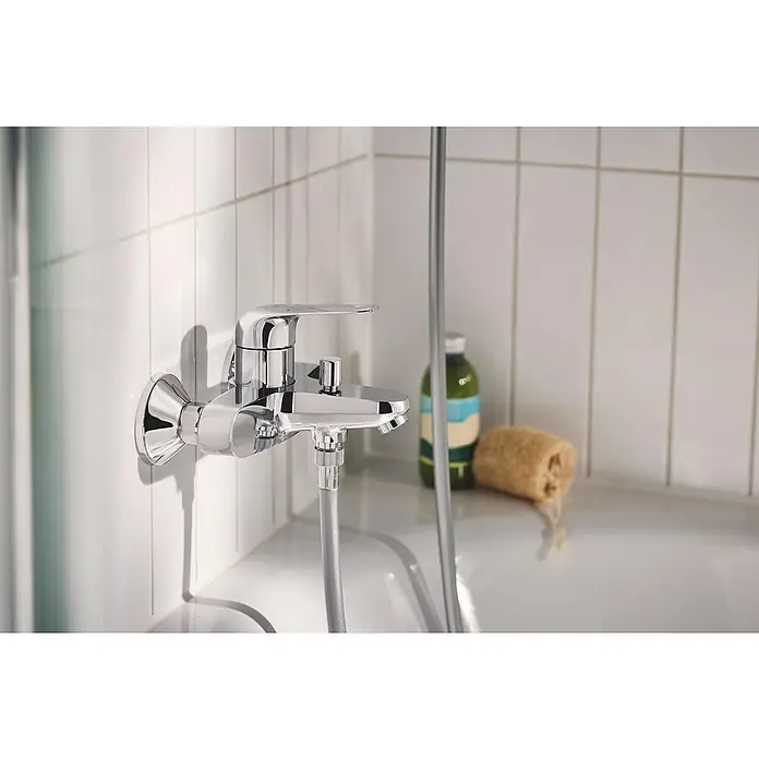 Grohe QuickFix Badewannenarmatur Swift - Chrom, Funkelnd - Nahaufnahme eines glänzenden, verchromten Badewannenmischers mit Brausegarnitur an einer weißen Wand.
