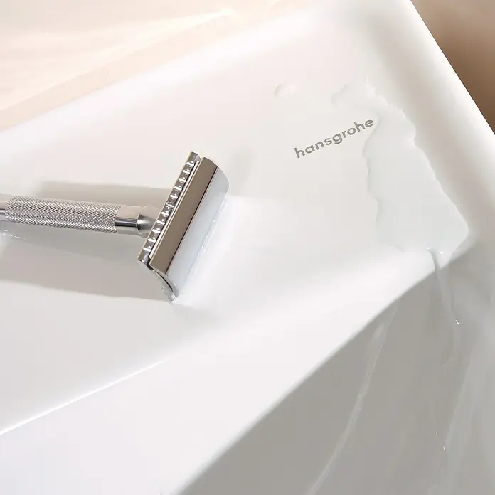 Hansgrohe Waschtisch Xanuia Q - B x L: 60 x 48 cm, Hahnloch: Mitte, Mit Überlauf, Weiß - Nahaufnahme eines glänzenden Rasierers auf einem weißen Waschbecken, neben dem Hansgrohe-Logo, das Eleganz und Funktionalität vereint.