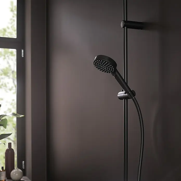 Hansgrohe Vernis Blend Handbrause Vario Eco - Anzahl Funktionen: 2 Stk., Durchmesser: 10 cm, Schwarz - Schwarze Handbrause mit Brauseschlauch und Halterung vor dunkler Wand und Fenster. Elegantes Baddesign mit modernem Touch.