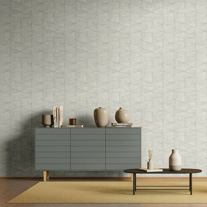 Marburg Travertino Papiertapete - Hellgrau, Grafisch, 10 x 0,53 m - Wohnzimmer-Interieur mit grauer Kommode, Deko-Vasen und Büchern auf einem gelben Teppich vor einer geometrischen Tapete.