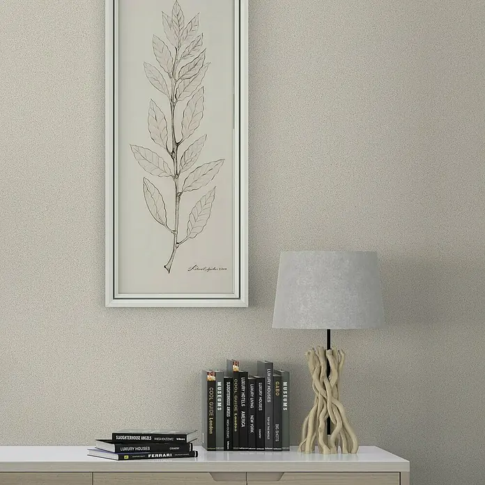 Marburg Travertino Vliestapete - Beige, Uni, 10,05 x 0,53 m - Stilleben mit einer stilvollen Lampe auf einem Stapel Bücher, ergänzt durch ein botanisches Wandbild und einen modernen Schrank.