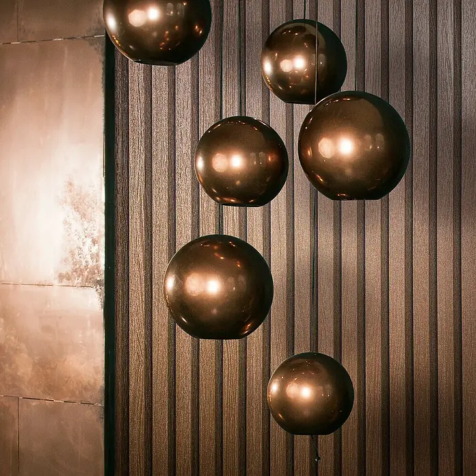 Marburg Travertino Vliestapete Paneel-Optik - Kupfer, Metalloptik, 10,05 x 0,53 m - Nahaufnahme von dekorativen Kupferkugelleuchten, die vor einer strukturierten Holzwand hängen und ein modernes, elegantes Ambiente schaffen.
