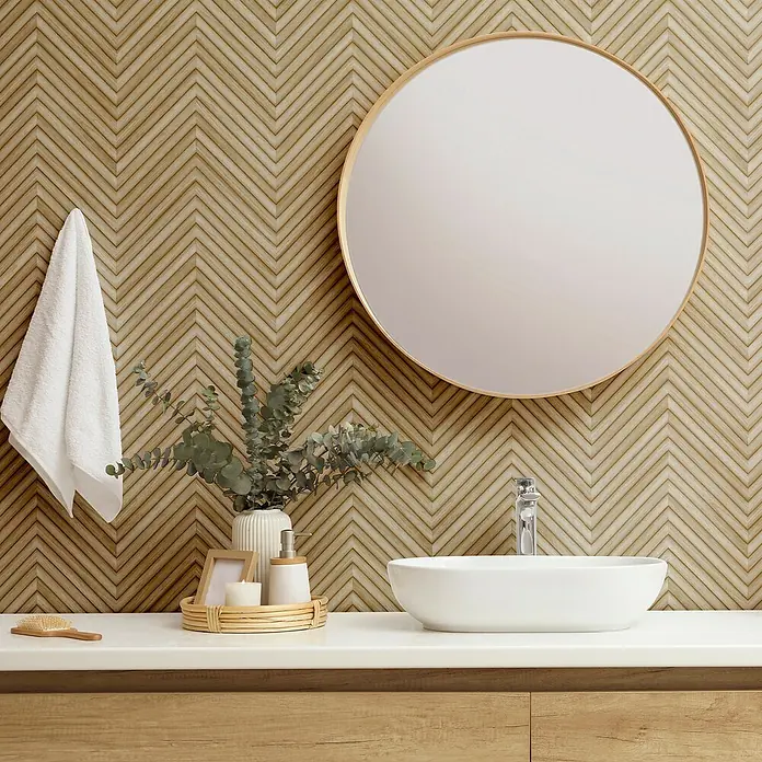 Marburg Travertino Vliestapete Fischgrätmuster - Beige, Holzoptik, 10,05 x 0,53 m - Badezimmerwaschtisch mit einem runden Spiegel, einer weißen Schale und einer stilvollen Armatur vor einer Wand mit Chevron-Muster.
