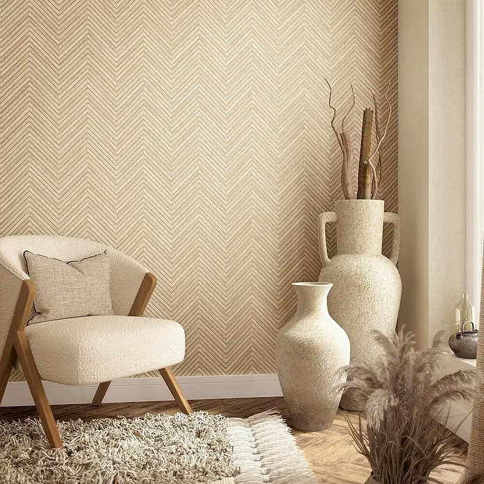 Marburg Travertino Vliestapete Fischgrätmuster - Beige, Holzoptik, 10,05 x 0,53 m - Gemütliches Wohnzimmer mit beigem Sessel, Zickzack-Tapete und dekorativen Vasen. Ein stilvoller Teppich rundet das Ambiente ab.