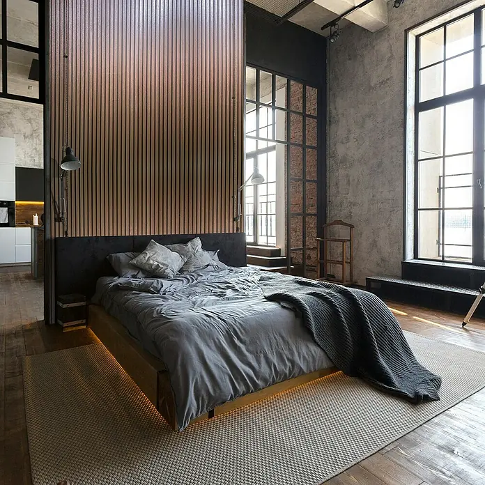Marburg Travertino Vliestapete Paneel-Optik - Kupfer, Metalloptik, 10,05 x 0,53 m - Einladendes Schlafzimmer im Loft-Stil mit großem Bett, Holzwand und industriellem Design, das zum Entspannen einlädt.