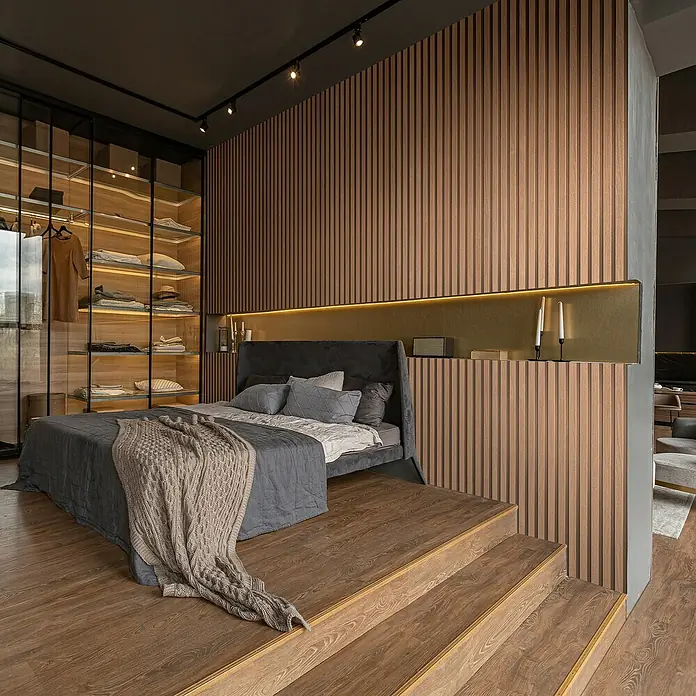 Marburg Travertino Vliestapete Paneel-Optik - Kupfer, Metalloptik, 10,05 x 0,53 m - Elegantes Schlafzimmer mit großem Bett, Holzpaneelen und begehbarem Kleiderschrank, das eine harmonische und luxuriöse Raumatmosphäre schafft.