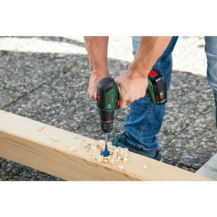 Bosch Power for All 18V Akku-Bohrschrauber AdvancedDrill 18V-80 QuickSnap - 18 V, 1 Akku, 2,5 Ah, 78 Nm - Ein Mann bohrt mit einem grünen Bosch Akku-Bohrschrauber ein Loch in ein Holzbrett, wobei Späne entstehen.