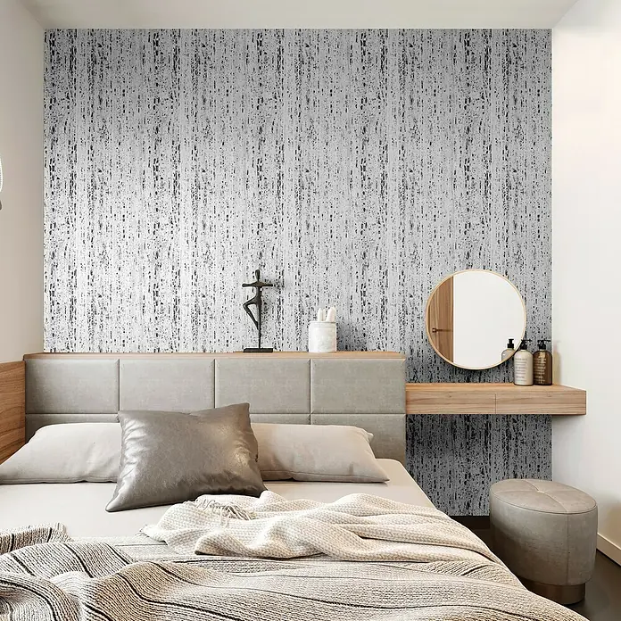 Marburg Travertino Vliestapete Struktur - Hellgrau-Grau, Steinoptik, 10,05 x 0,53 m - Ein Schlafzimmer mit stilvoller Dekoration, inklusive einem bequemen Bett, einem Spiegel und einem Hocker. Die graue Tapete verleiht dem Raum Eleganz.