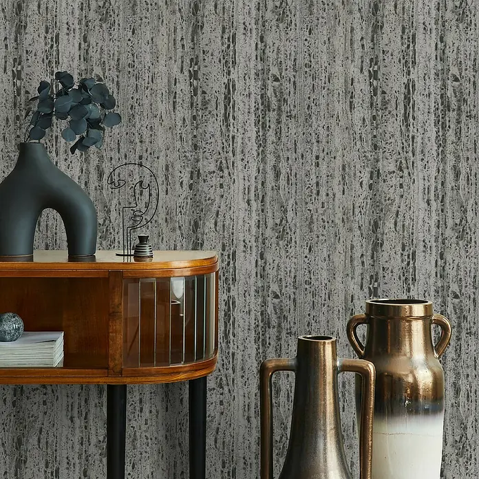 Marburg Travertino Vliestapete Struktur - Braun-Grau, Steinoptik, 10,05 x 0,53 m - Dekorative Szene mit stilvollen Vasen und einem eleganten Schrank vor einer strukturierten Wand, die dem Raum eine künstlerische Note verleiht.