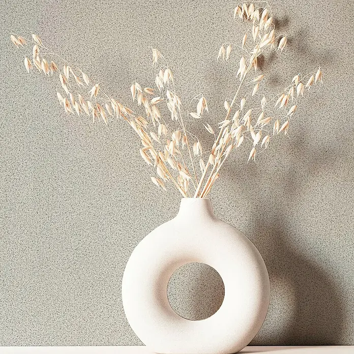 Marburg Travertino Vliestapete - Braungrau, Uni, 10,05 x 0,53 m - Stillleben mit einer modernen Donut-Vase aus Keramik und Trockenblumen, die eine elegante und minimalistische Ästhetik erzeugt.