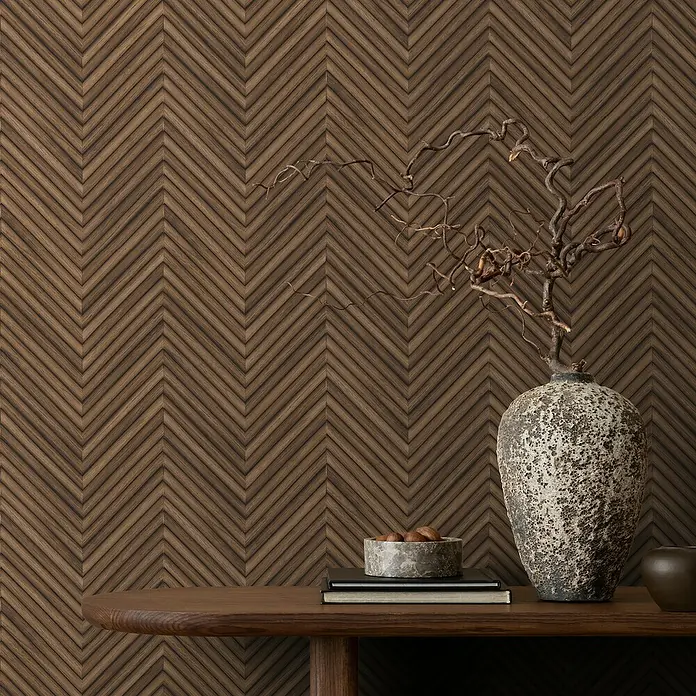 Marburg Travertino Vliestapete Fischgrätmuster - Dunkelbraun, Holzoptik, 10,05 x 0,53 m - Dekorative Tischszene mit einer rustikalen Vase, Büchern und einer Schale, die auf einem eleganten Holztisch vor einer stilvollen Holzpaneelwand stehen.