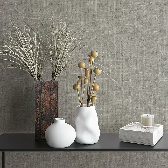Marburg Travertino Vliestapete - Strukturgrau, Uni, 10,05 x 0,53 m - Dekorative Komposition mit einer braunen Vase mit Federn, einer weißen Vase mit Holzdekoration, einer Kugelvase, Büchern und einer Kerze.