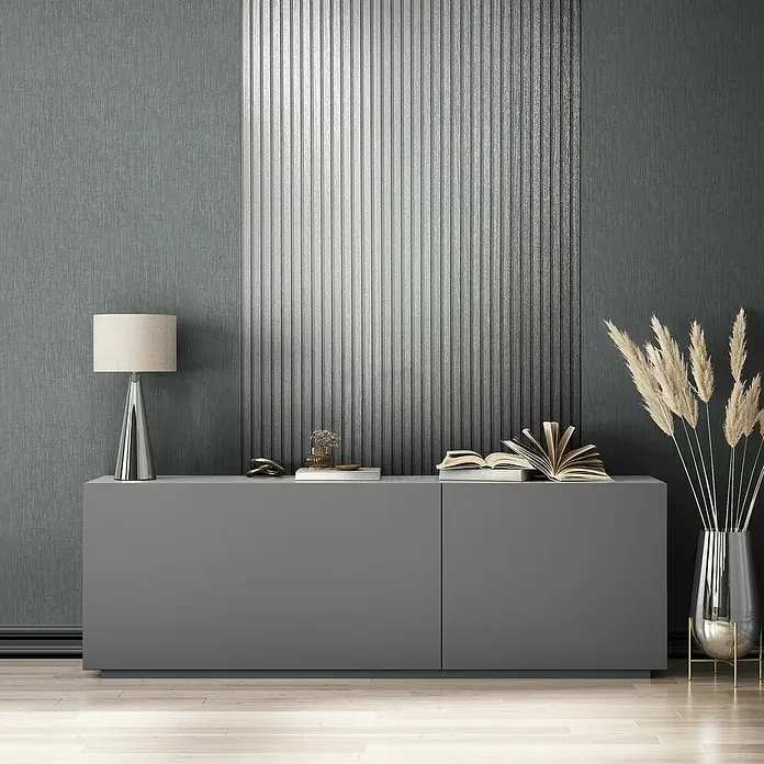 Marburg Travertino Vliestapete Paneel-Optik - Silber, Metalloptik, 10,05 x 0,53 m - Eine graue Kommode mit Dekorationsgegenständen wie einer Lampe, Büchern und einer Vase mit Pampasgras vor einer strukturierten Wand.