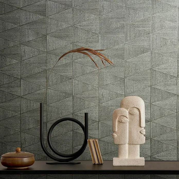 Marburg Travertino Papiertapete - Grau, Grafisch, 10,05 x 0,53 m - Dekorative Nahaufnahme mit einer Skulptur, einer modernen Vase, einem kleinen Buch und einer Dose auf einer schwarzen Oberfläche vor einer Wand mit dreieckigem Muster.