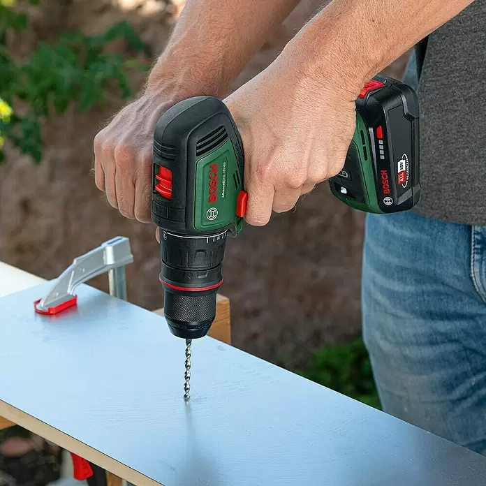 Bosch Power for All 18V Taladro atornillador de batería AdvancedDrill 18V-80 - 18 V, 2 baterías, 2,5 Ah, 78 Nm - Una persona usa un taladro inalámbrico Bosch negro y verde con una broca plateada para perforar una lámina de metal gris.