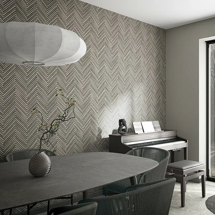Marburg Travertino Vliestapete Fischgrätmuster - Dunkelgrau, Holzoptik, 10,05 x 0,53 m - Esszimmer mit modernem Esstisch, Stühlen und einem Digitalpiano vor einer gemusterten Wand. Eine stilvolle Pendelleuchte hängt über dem Tisch.