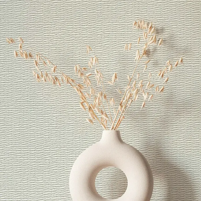 Marburg Travertino Vliestapete Textiloptik - Hellbeige, Sonstiges, 10,05 x 0,53 m - Elegante Nahaufnahme einer modernen, kreisförmigen Vase mit filigranen getrockneten Blumen vor einem strukturierten Hintergrund.