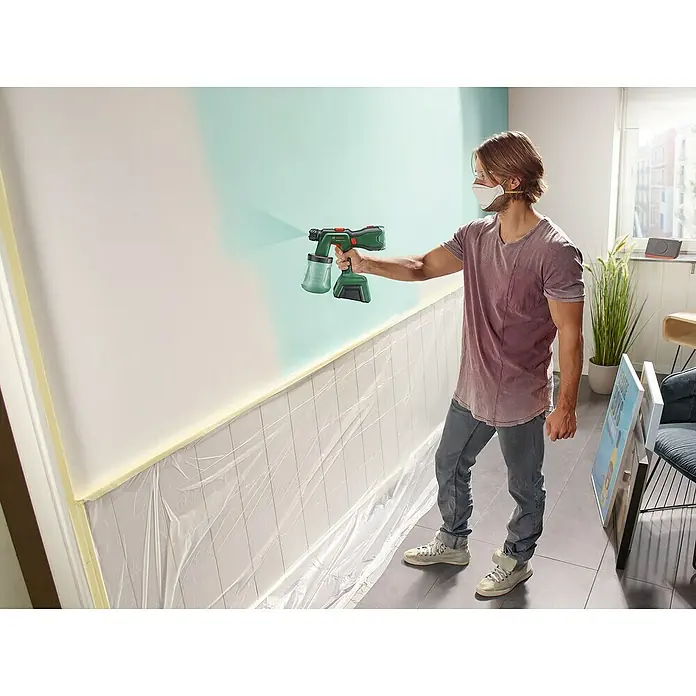 Bosch Power for All 18V Akku-Farbsprühsystem AdvancedSpray 18V-500 - 18 V, 1 Akku, 4 Ah, Max. Fördermenge: 0,5 l/min - Ein Mann sprüht Farbe mit einem Bosch Farbsprühsystem an eine Wand, die teilweise mit Folie abgedeckt ist.