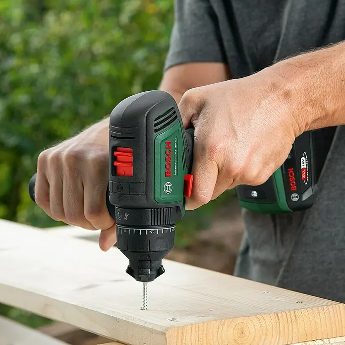 Bosch Power for All 18V Akku-Schlagbohrschrauber AdvancedImpact 18V-80 QuickSnap - 18 V, 2 Akkus, 2,5 Ah, 82 Nm - Nahaufnahme eines Mannes, der mit einem Bosch AdvancedImpact 18V-80 Akku-Bohrschrauber eine Schraube in ein Holzbrett dreht.