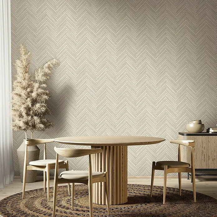 Marburg Travertino Vliestapete Fischgrätmuster - Weißbeige, Holzoptik, 10,05 x 0,53 m - Ein Esszimmer mit einem runden Holztisch, Stühlen, einem Schrank und einer hohen Pflanze vor einer Wand mit Zickzackmuster.