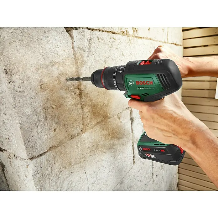 Bosch Power for All 18V Akku-Schlagbohrschrauber AdvancedImpact 18V-80 QuickSnap - 18 V, 2 Akkus, 2,5 Ah, 82 Nm - Ein Mann bohrt mit einem grünen Bosch Akku-Bohrschrauber ein Loch in eine Steinwand.