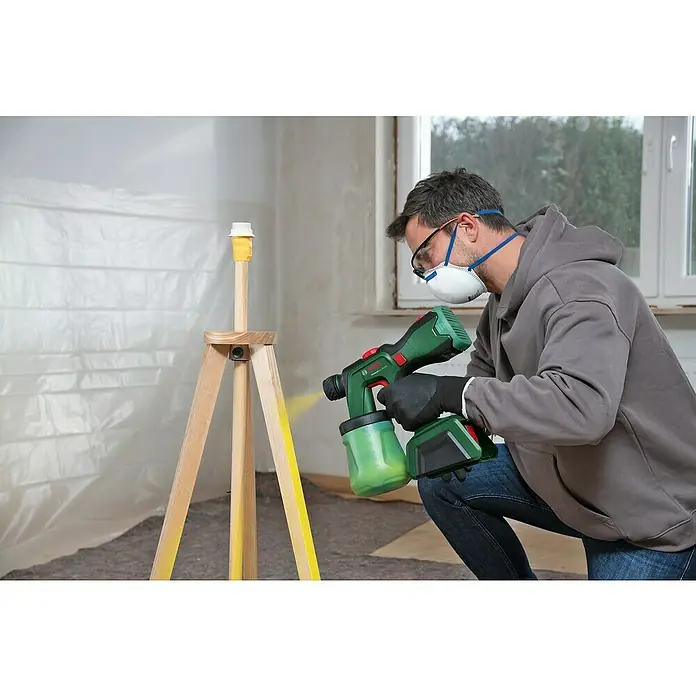 Bosch Power for All 18V Akku-Farbsprühsystem AdvancedSpray 18V-500 - 18 V, 1 Akku, 4 Ah, Max. Fördermenge: 0,5 l/min - Mann benutzt eine Bosch Farbspritzpistole, um einen Holzgegenstand gelb zu streichen. Die Farbspritzpistole ist grün und schwarz und hat einen Akku.
