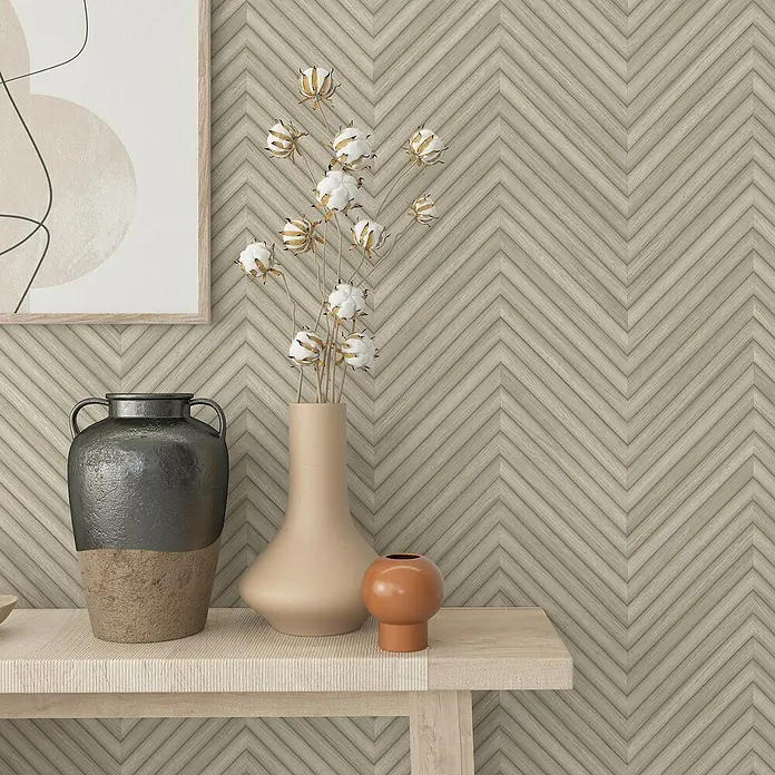 Marburg Travertino Vliestapete Fischgrätmuster - Weißbeige, Holzoptik, 10,05 x 0,53 m - Stillleben mit Vasen und einem gerahmten Kunstwerk auf einem hellen Holztisch vor einer Holzwand im Fischgrätenmuster.