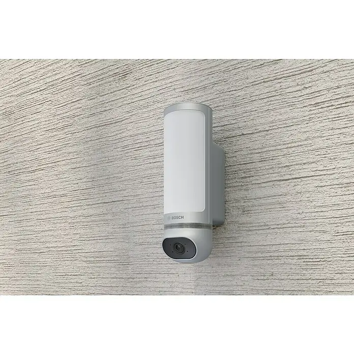 Bosch Smart Home Außenkamera Eyes II - 1.080 Pixel (Full HD), Silber, Erfassungswinkel: 180 °, Erfassungsreichweite: 8 m - Nahaufnahme einer Bosch Sicherheitskamera mit integrierter Lampe, die an einer strukturierten Wand montiert ist.