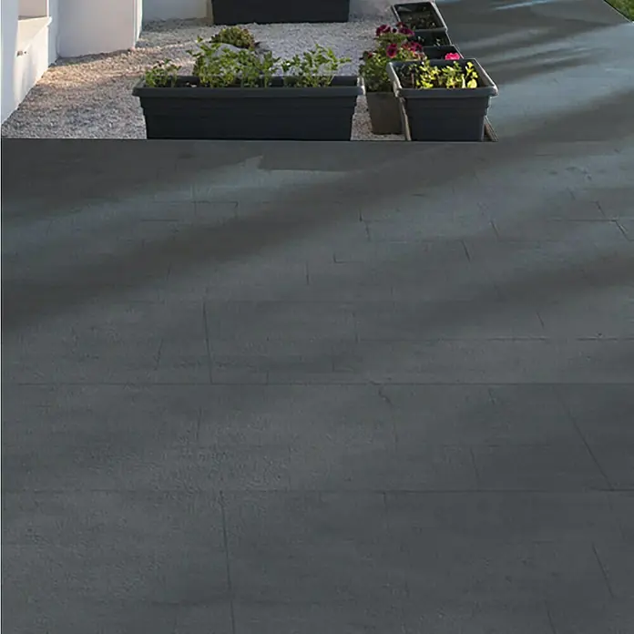 Terrassenfliese Revesto 2.0 - 60 x 60 x 2 cm, Anthrazit, Matt - Eine Reihe von Pflanzkästen mit üppigem Grün und bunten Blumen säumen einen gepflasterten Bereich im Freien.