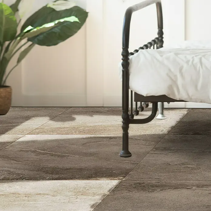 Terrassenfliese Aspen 2.0 - 60 x 60 x 2 cm, Braun, Matt - Nahaufnahme eines Bodens mit braunen Fliesen und einem Bettgestell. Die Fliesen präsentieren ein elegantes, natürliches Design.