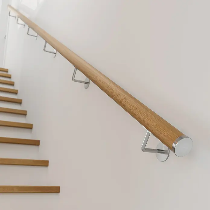 Dolle Endkappe PS 913Edelstahl V2A, 2 Stk., Passend für: Dolle Holzhandläufe Ø 50 mm - Holzhandlauf mit Halterungen an einer weißen Wand neben einer Treppe. Das Geländer bietet Sicherheit beim Treppensteigen.