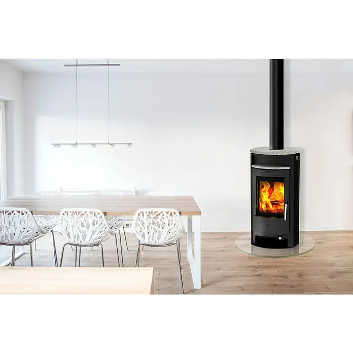 Fireplace Kaminofen Burma - 6 kW, Raumheizvermögen: 108 m³, Material Verkleidung: Speckstein, Schwarz - Bild eines Kaminofens mit schwarzem Gehäuse und Glasplatte in einem hellen Raum mit Holzboden.