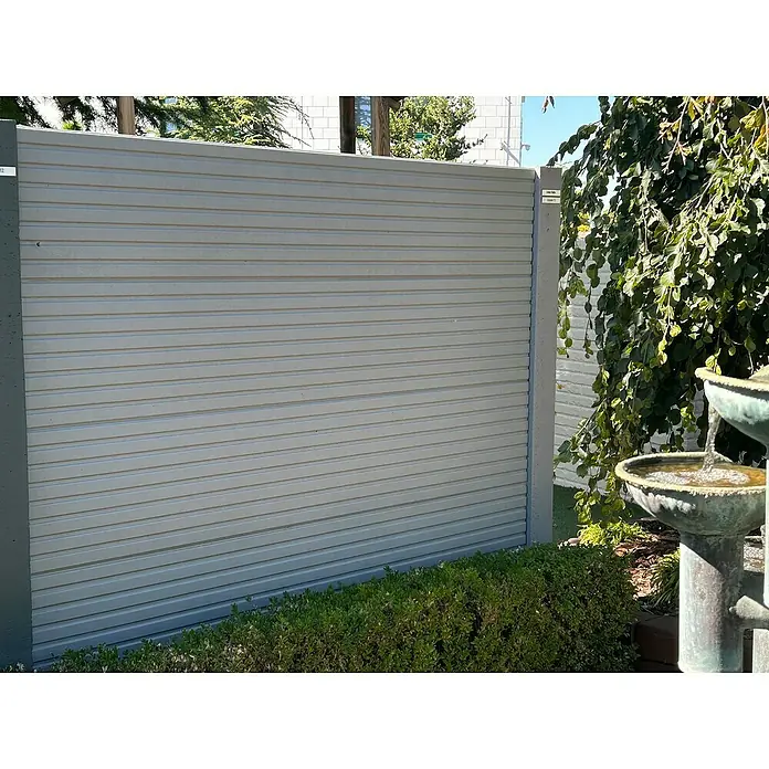 Beckers Betonzaun Zaunelement Klassik Linear Motiv - 200 x 38,5 cm, Beton, Betongrau - Diese Nahaufnahme zeigt ein modernes, graues Zaunelement mit horizontalen Linien und Betonpfosten, umgeben von Grünpflanzen und einem Brunnen.