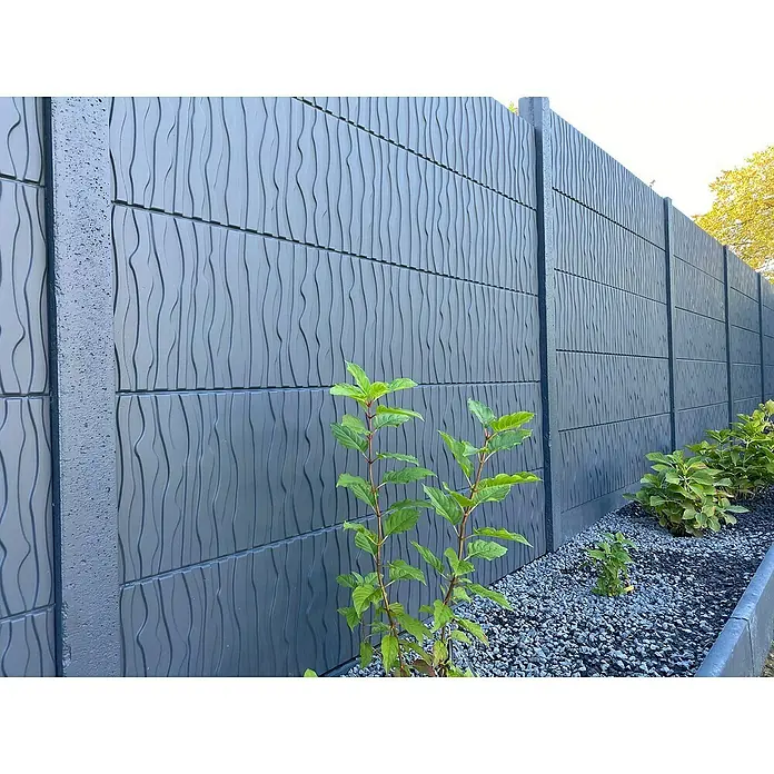 Beckers Betonzaun Zaunelement Standard River Motiv - 200 x 38,5 cm, Beton, Betongrau - Nahaufnahme eines grauen Betonzauns mit vertikalen Rillen, umgeben von grünen Pflanzen und Kies. Moderner, strukturierter Gartenzaun.