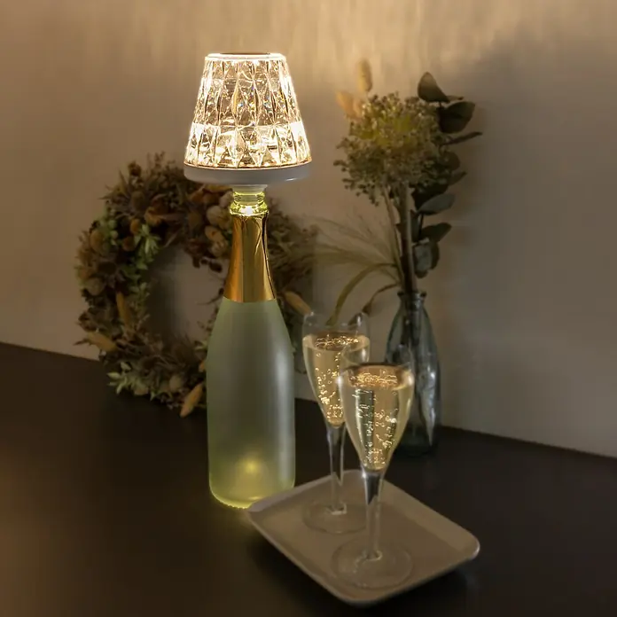 REV LED-Flaschenleuchte Lamprusco Cristal - 2 W, Weiß, Warmweiß - Elegante Szene mit einer Flasche, die als Lampenfuß dient, zwei Gläsern Champagner und dekorativen Elementen, die eine festliche Atmosphäre schaffen.