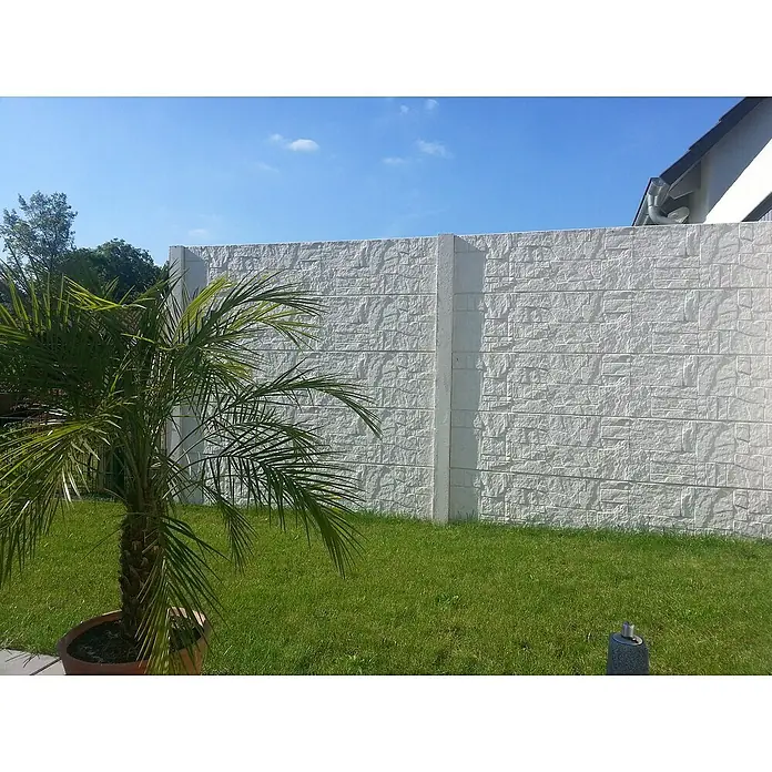 Beckers Betonzaun Zaunelement Standard Flagstone Motiv - 200 x 38,5 cm, Beton, Betongrau - Eine weiße, strukturierte Gartenmauer dient als stilvoller Hintergrund für einen Topf mit einer kleinen Palme, umgeben von Rasen.