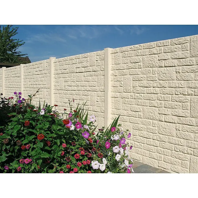 Beckers Betonzaun Zaunelement Klassik Romania Motiv - Beton, Betongrau - Eine lange, weiße Steinmauer mit blühenden Blumen im Vordergrund, die einen farbenfrohen Akzent setzt. Eine schöne Gartengestaltung.