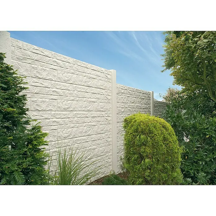 Beckers Betonzaun Zaunelement Klassik Fels Motiv - 184 x 26 cm, Beton, Betongrau - Bild einer grauen Steinmauer mit weißen Pfosten und üppigem Grün. Die Mauer dient als stilvolle und dauerhafte Grundstücksbegrenzung.