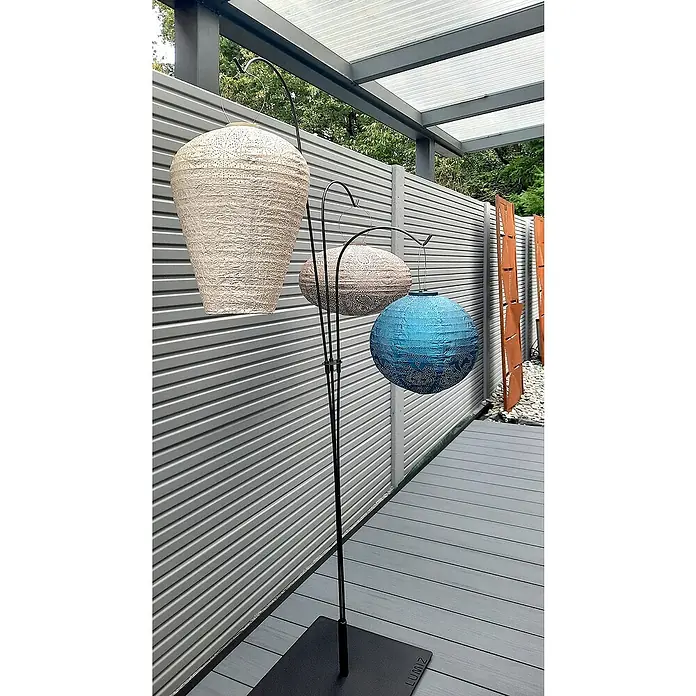 Beckers Betonzaun Zaunelement Klassik Linear Motiv - 184 x 26 cm, Beton, Betongrau - Ein dekorativer Außenbereich mit einer eleganten dreifachen Laternenstange, die farbige Papierlaternen in verschiedenen Formen und Größen trägt.