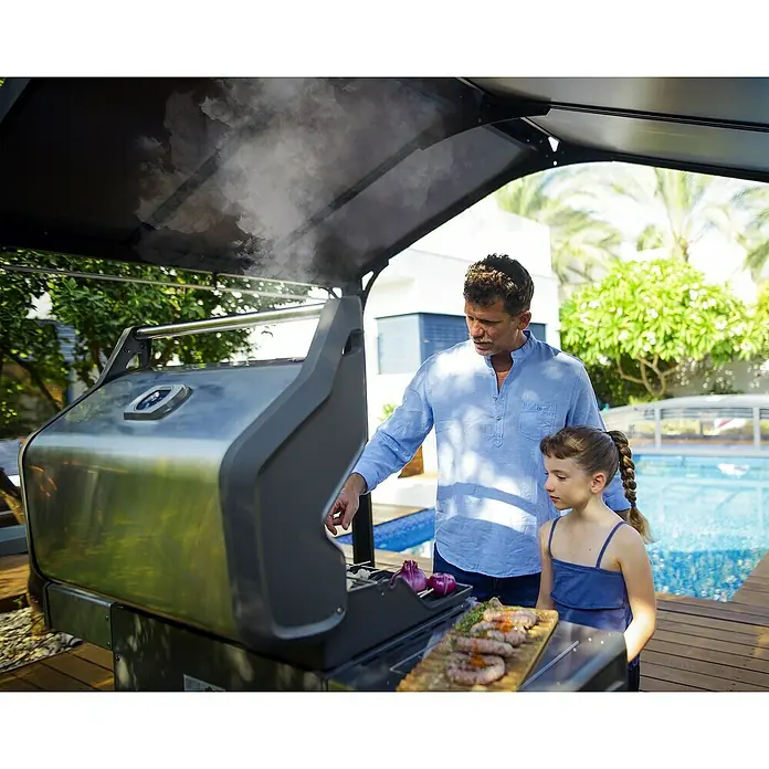Palram – Canopia Pérgola para barbacoa Austin - An x Pr: 240 x 180 cm, Color del armazón: Antracita, Aluminio - Un hombre asa salchichas en una parrilla moderna, con una joven a su lado admirando la comida.