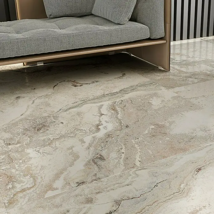 Feinsteinzeugfliese Phantasia - 60 x 120 cm, Beige, Matt - Nahaufnahme eines modernen Sofas mit hellgrauem Kissen auf einem gemusterten, marmorierten Boden.