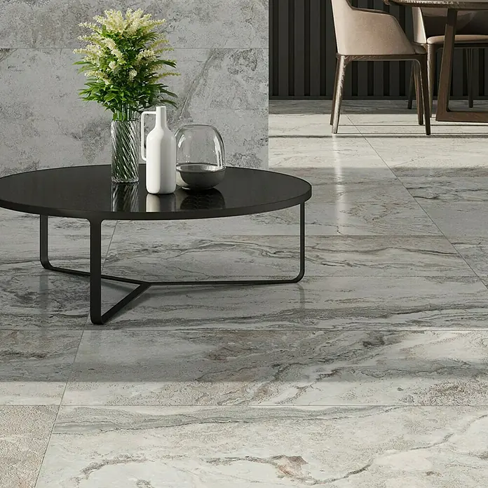 Feinsteinzeugfliese Phantasia - 60 x 120 cm, Grau, Matt - Ein runder, schwarzer Couchtisch mit Blumen und Dekorationsgegenständen darauf, im Vordergrund des Fliesenbodens.