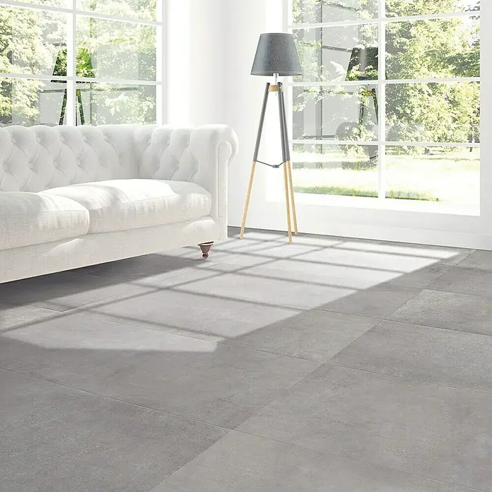 Feinsteinzeugfliese Rimini - 60 x 120 cm, Grigio, Matt - Ein elegantes Wohnzimmer mit grauen Bodenfliesen, einem weißen Sofa und einer stilvollen Stehlampe vor dem Fenster.