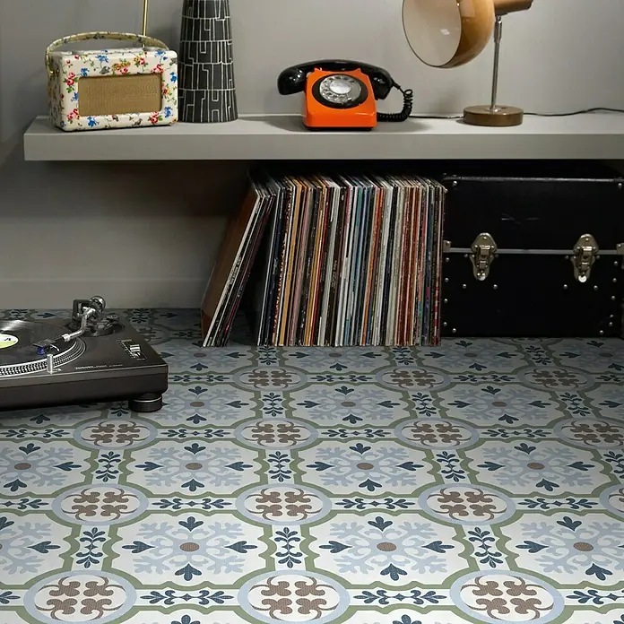 Feinsteinzeugfliese Cordoba Posada - 24,8 x 24,8 cm, Bunt, Matt - Ein Plattenspieler steht auf einem Fliesenboden mit Retro-Muster, umgeben von Schallplatten und Vintage-Dekorationen auf einem Regal.