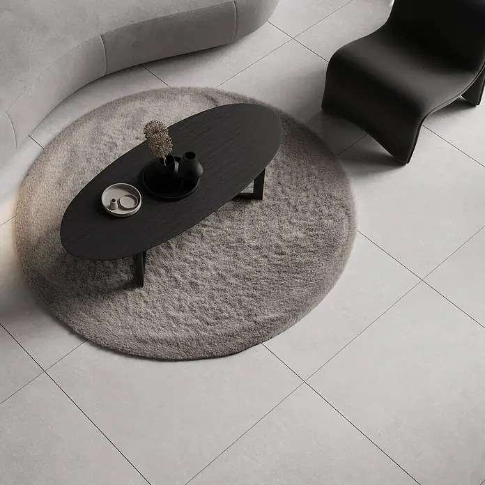 Feinsteinzeugfliese Giant - 79,7 x 79,7 cm, Weiß, Matt - Ansicht von oben auf einen schwarzen ovalen Couchtisch auf einem grauen runden Teppich, mit dekorativen Accessoires und einem modernen Stuhl.