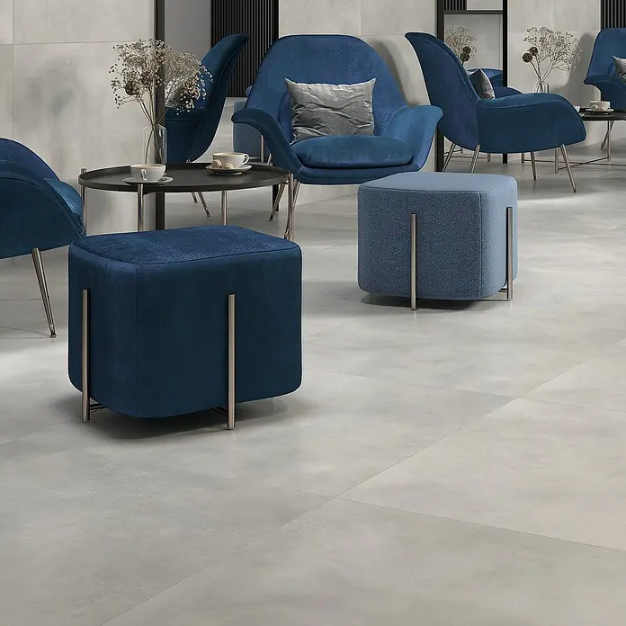 Feinsteinzeugfliese Dimension - 79,7 x 79,7 cm, Grau, Matt - Blauer, würfelförmiger Pouf mit Metallbeinen in einem stilvollen Wartebereich, ergänzt durch blaue Sessel und einen kleinen Tisch.