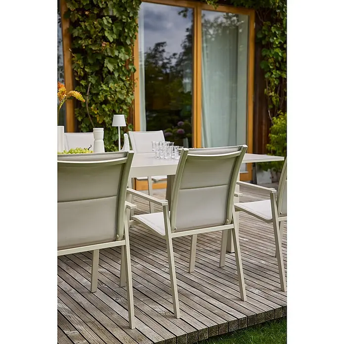 Sunfun Maja Stapelsessel - Aluminium, Stapelbar, Light-Greige, B x T x H: 56,5 x 66 x 91 cm - Gartensitzgruppe mit hellen Stühlen und Tisch auf einer Holzterrasse, ideal für entspannte Stunden im Freien, umgeben von üppigem Grün.